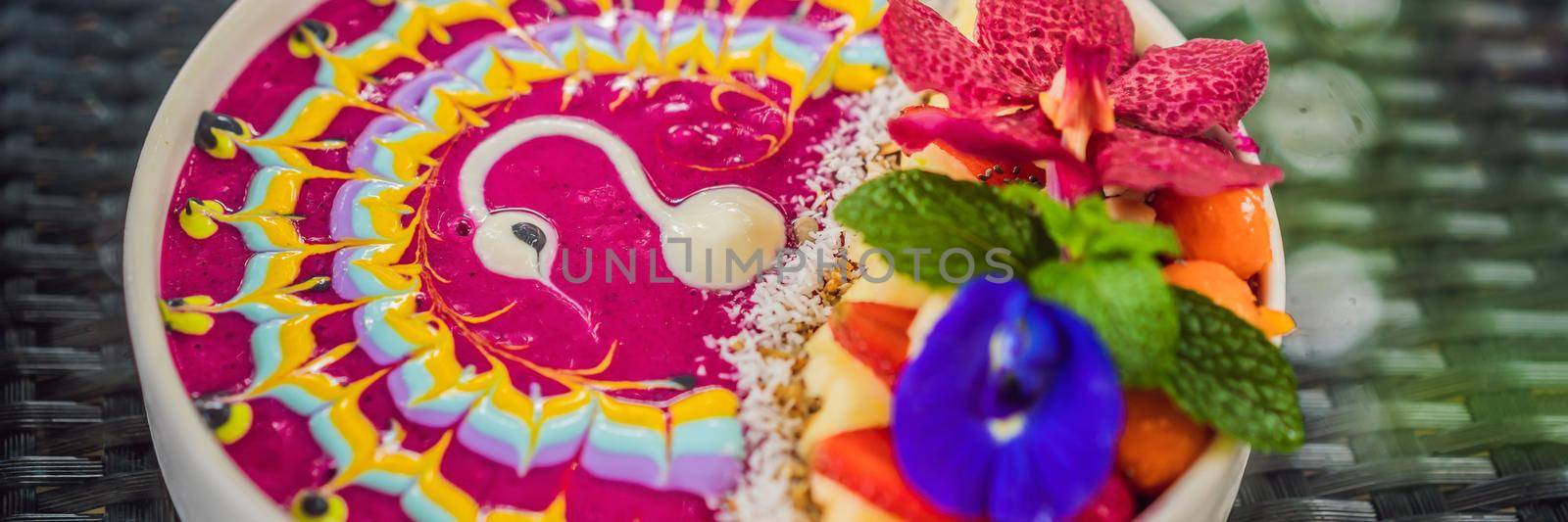 BANNER, LONG FORMAT Healthy tropical breakfast, smoothie bowl with tropical fruits, decorated with a pattern of colorful yogurt with turmeric and spirulina. It is also decorated with fruits, flowers, chia seeds, coconut, granola, pineapple, mint and strawberries by galitskaya