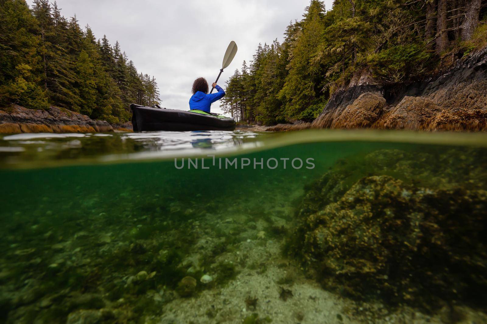 Over and Under picture of an Adventurous woman kayaking in the Pacific Ocean during a cloudy morning. Taken in Port Hardy, Vancouver Island, BC, Canada.
