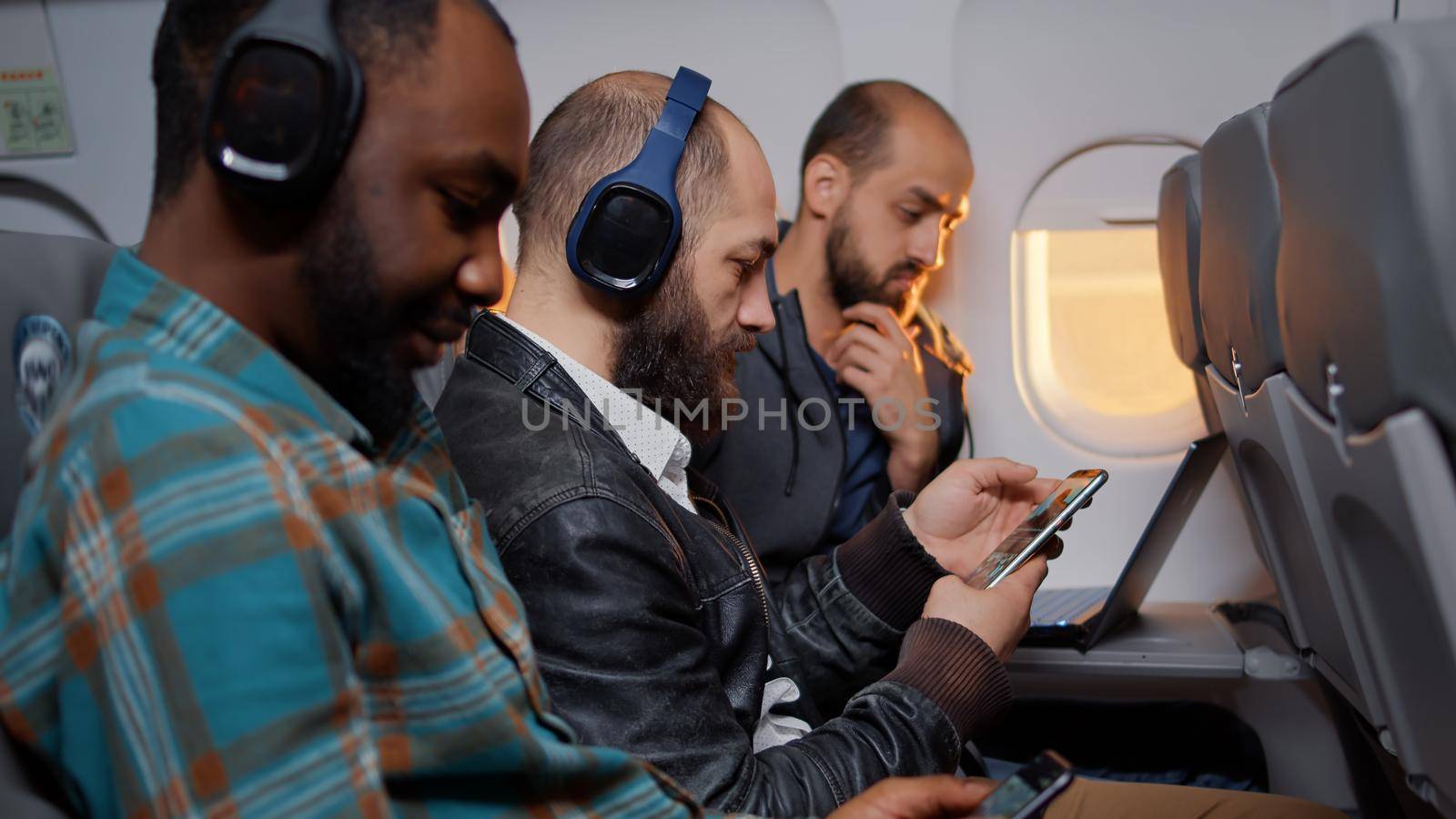 Male employee sitting on airplane flight during sunset by DCStudio