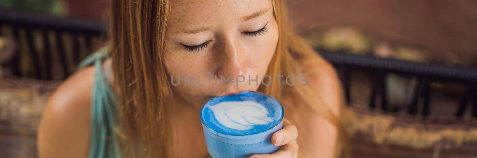 Young woman having a mediterranean breakfast seated at sofa and drinks Trendy drink: Blue latte. Hot butterfly pea latte or blue spirulina latte BANNER, LONG FORMAT by galitskaya