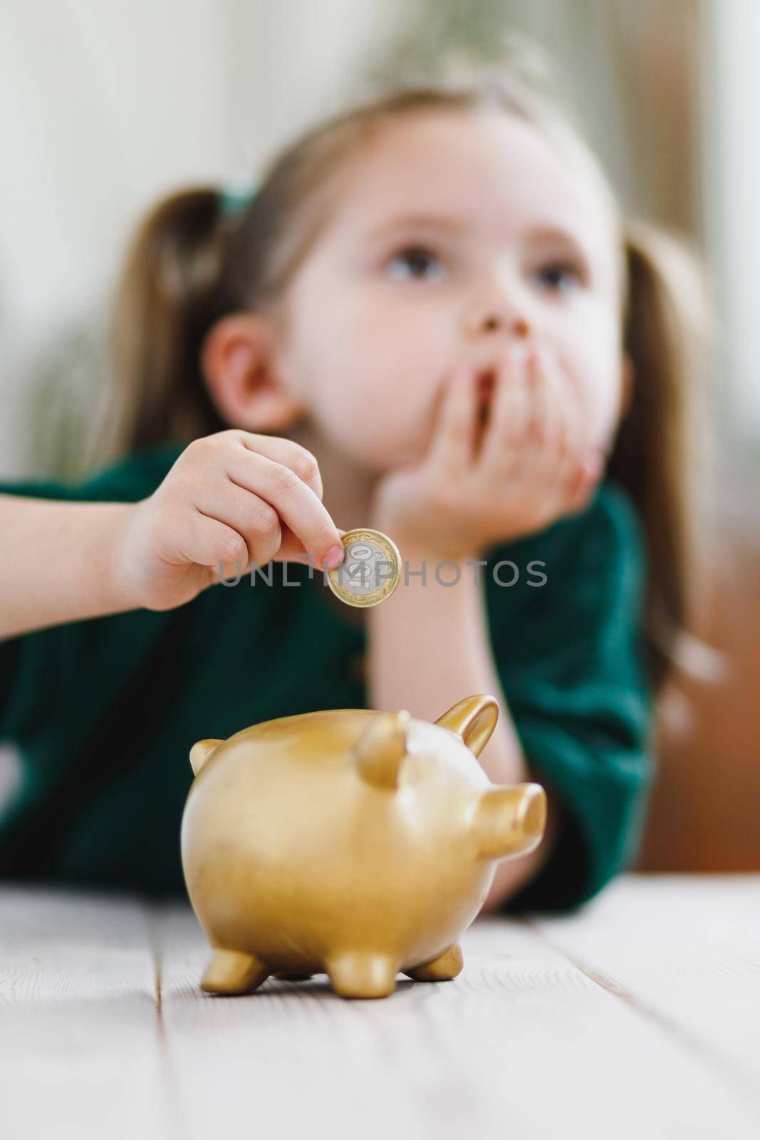 Little girl thinking about her money spending and putting a coin into a piggy bank. Economy, money saving and deposit concept. Selective soft focus