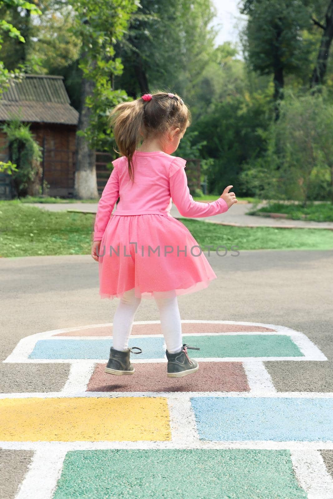 Little girl in a pink dress plays hopscotch on the street