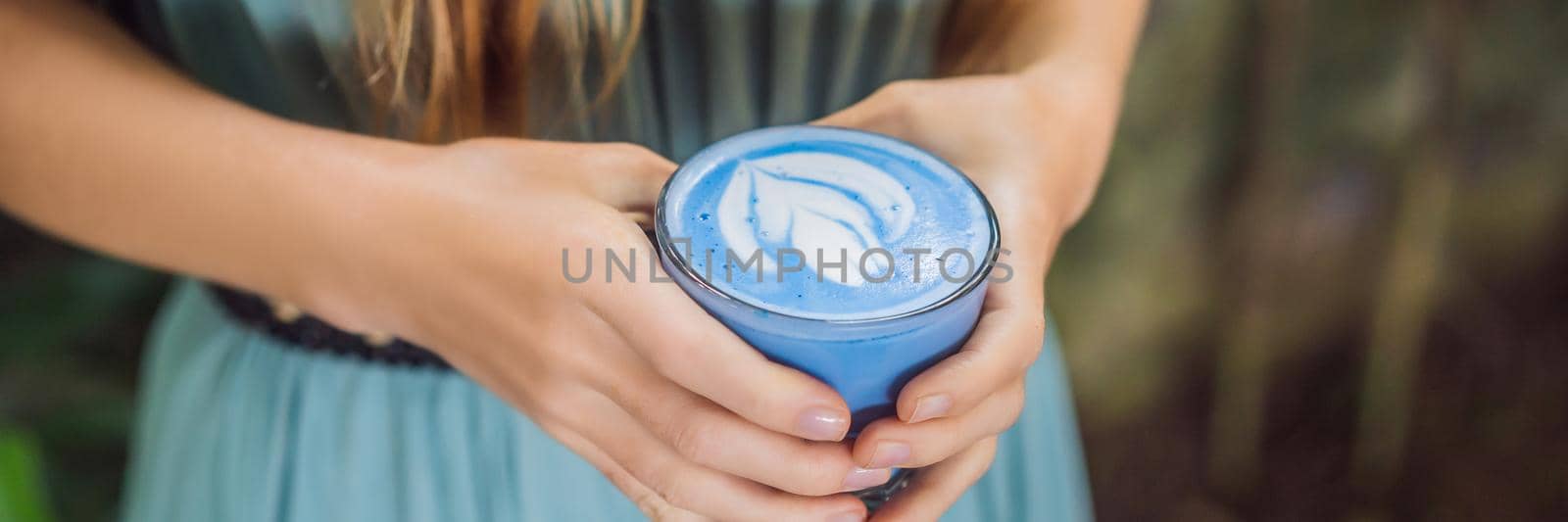 Young woman having a mediterranean breakfast seated at sofa and drinks Trendy drink: Blue latte. Hot butterfly pea latte or blue spirulina latte. BANNER, LONG FORMAT