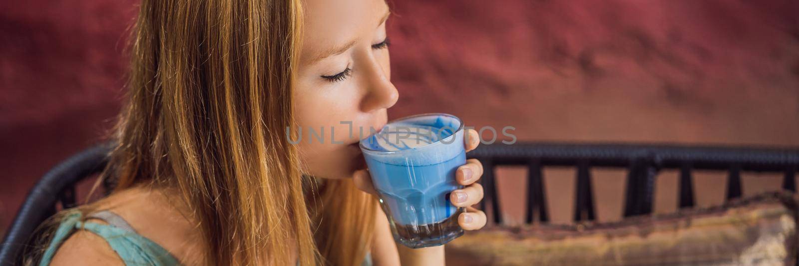 Young woman having a mediterranean breakfast seated at sofa and drinks Trendy drink: Blue latte. Hot butterfly pea latte or blue spirulina latte BANNER, LONG FORMAT by galitskaya