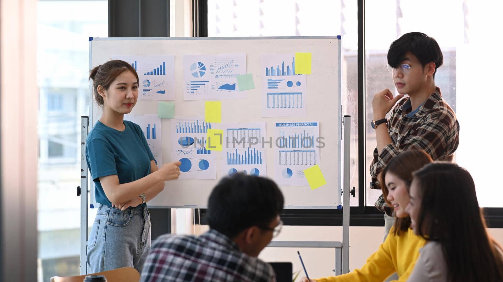 Confident woman standing near flip chart with her colleague and giving presenting new marketing strategy.