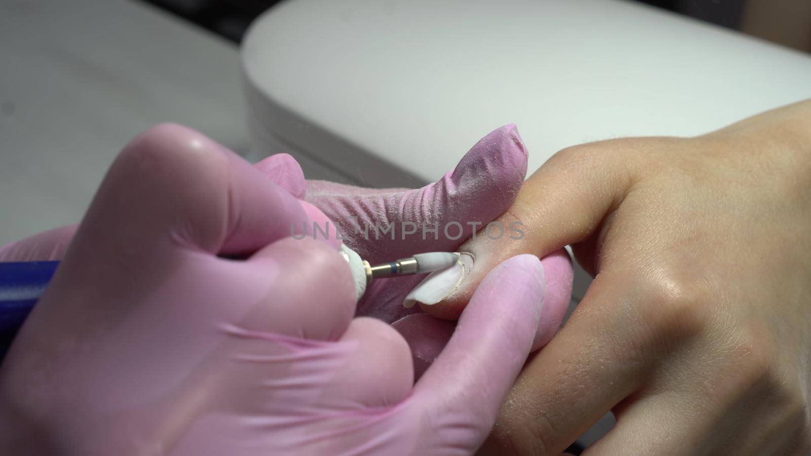 Young woman in the salon does a manicure. A manicurist uses a drill machine to remove nails. Closeup. 4k