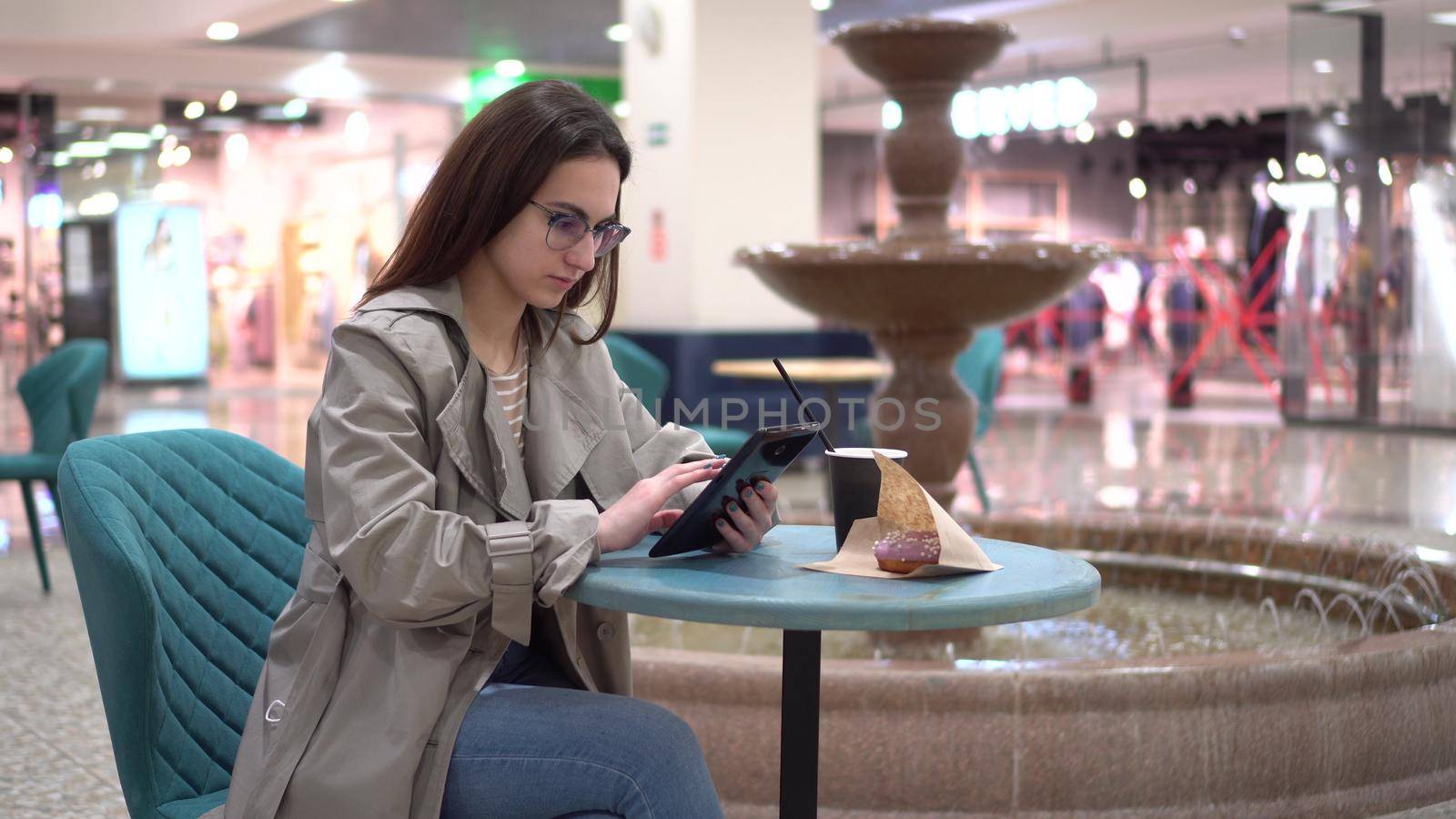 A young woman in a cafe with a tablet in her hands against the background of a fountain. Decoration in the cafe. 4k
