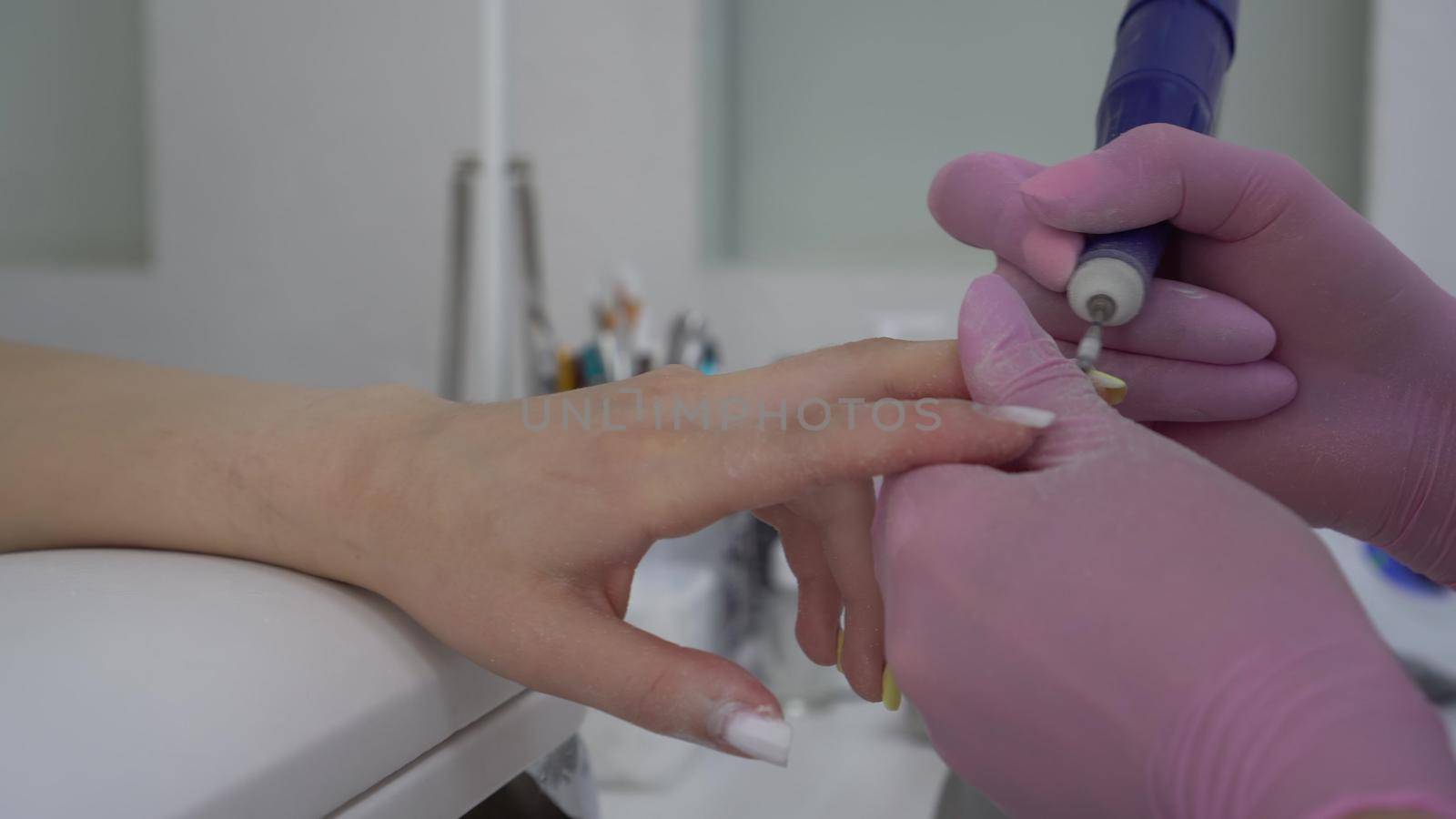 Young Asian woman with glasses in a manicure salon. A manicurist uses a drill machine to remove nails. by Puzankov