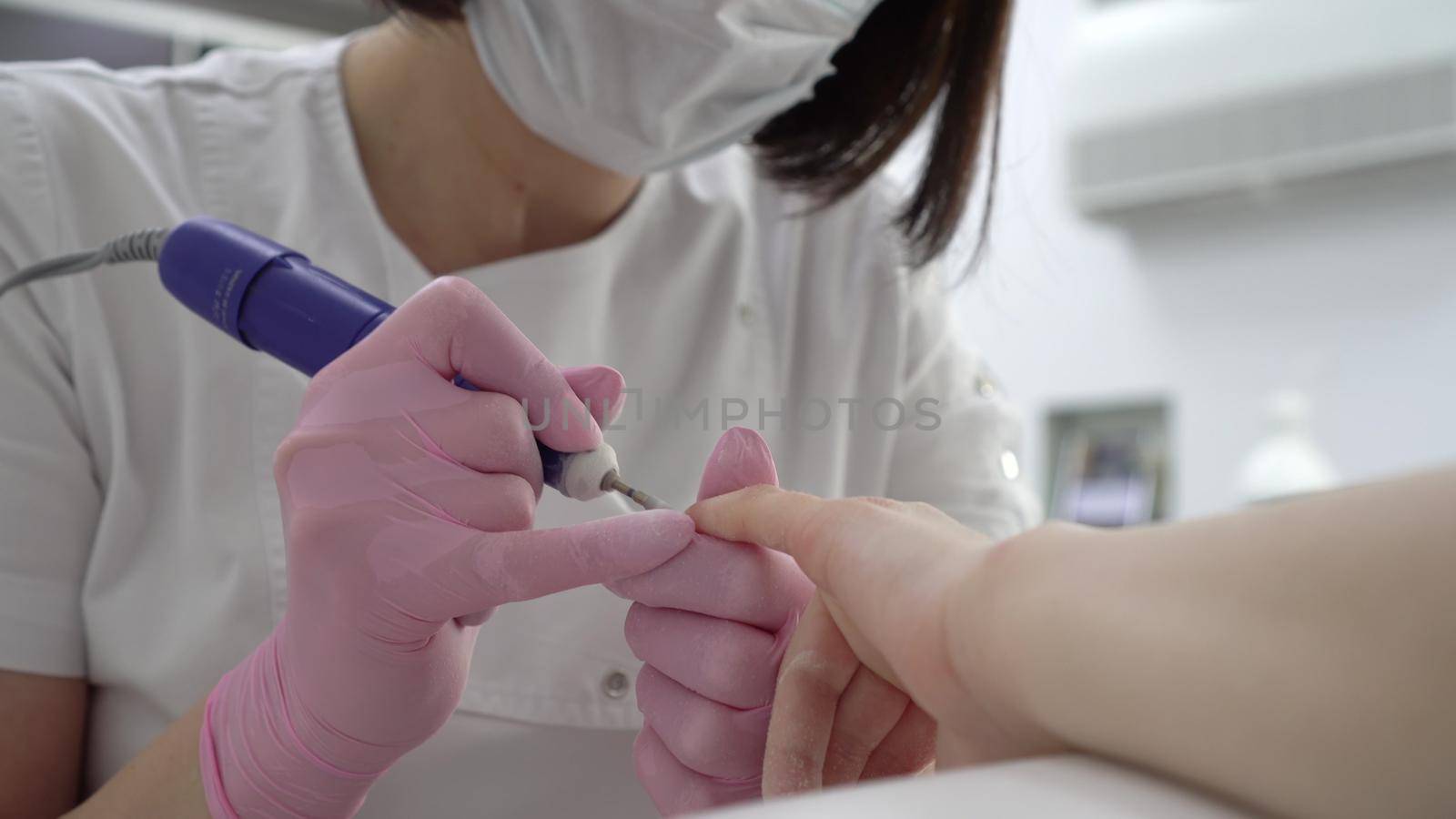 A professional manicurist using a drill tool cuts off old nails close-up. Nail care in a manicure salon. 4k