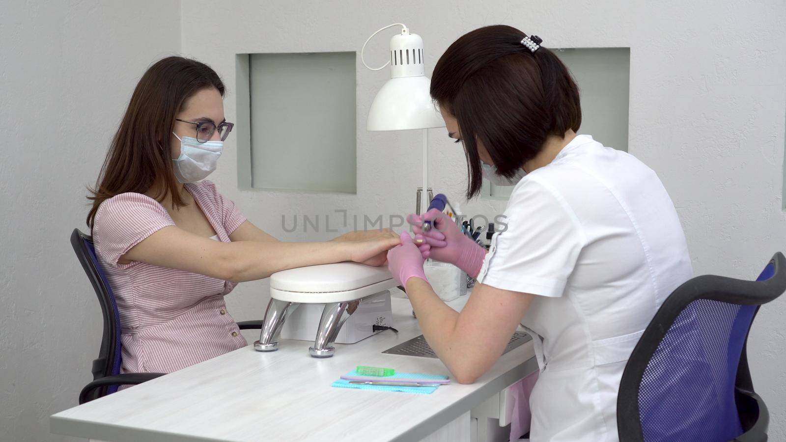 Young woman with glasses in a manicure salon. A manicurist uses a drill machine to remove nails. 4k