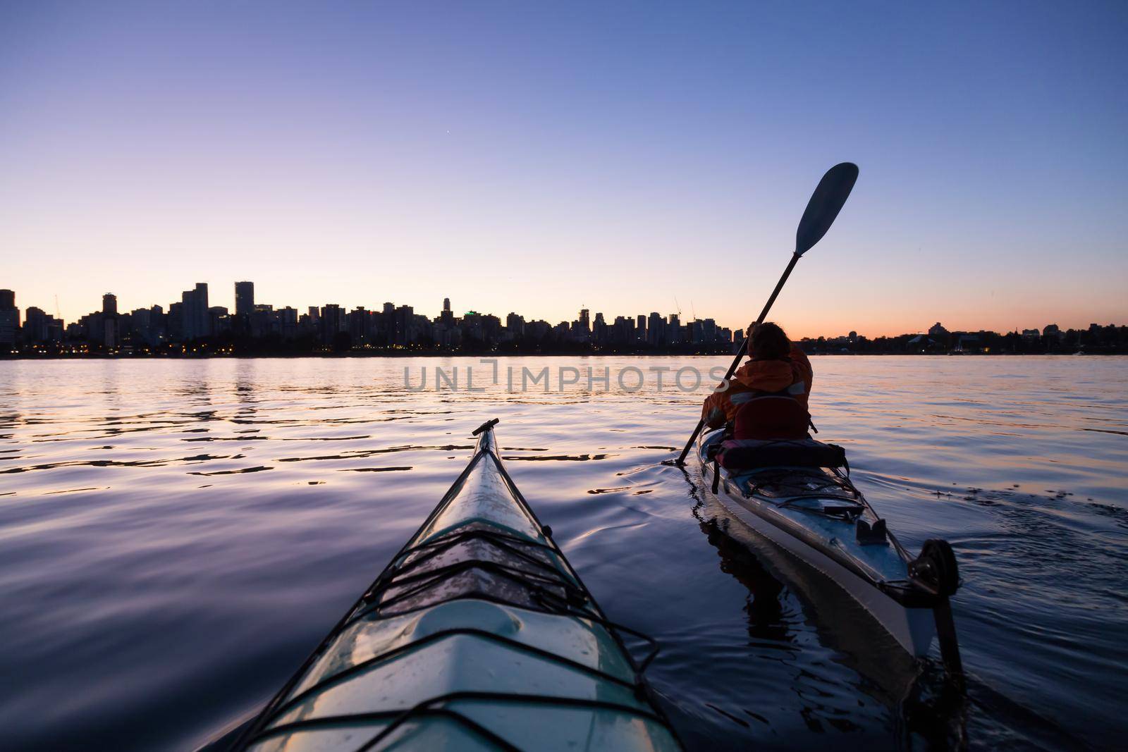 Sea Kayaking during a vibrant sunrise with the city skyline in the background. Taken in Downtown Vancouver, British Columbia, Canada.