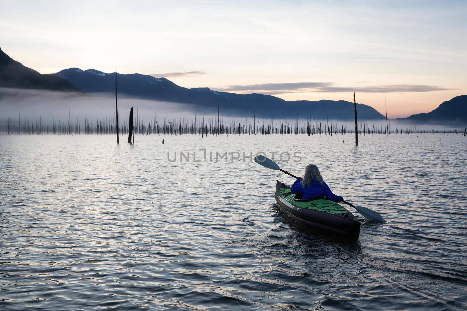 Adventurous Girl kayaking on an infatable kayak in a beautiful lake during a calm and peaceful sunrise. Taken in Stave Lake, East of Vancouver, British Columbia, Canada.