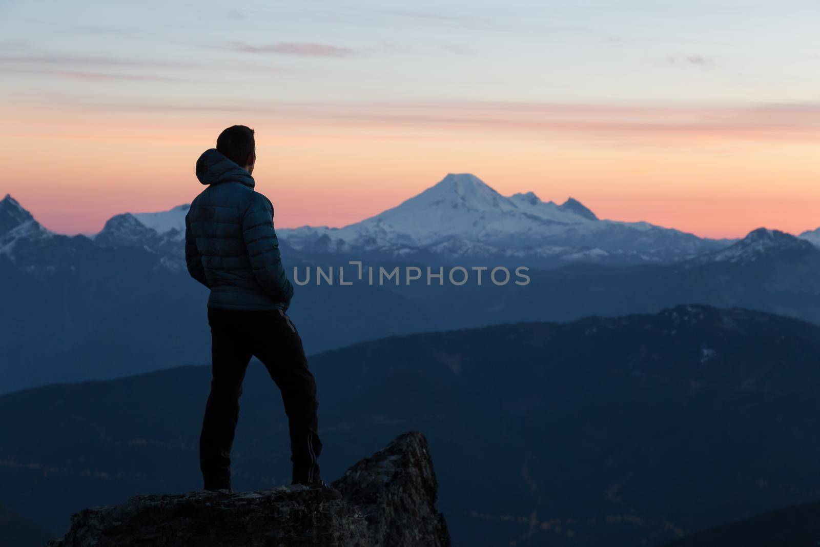 Adventurous man is standing on top of the mountain and enjoying the beautiful view during sunset. Taken on top of Cheam Peak in Chilliwack, East of Vancouver, BC, Canada.