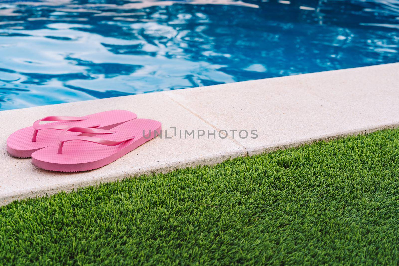 Pink flip flops for pool or beach on grass with pool bottom. Pool water texture. to use text. Natural light outside. Sunny day. summer objects.