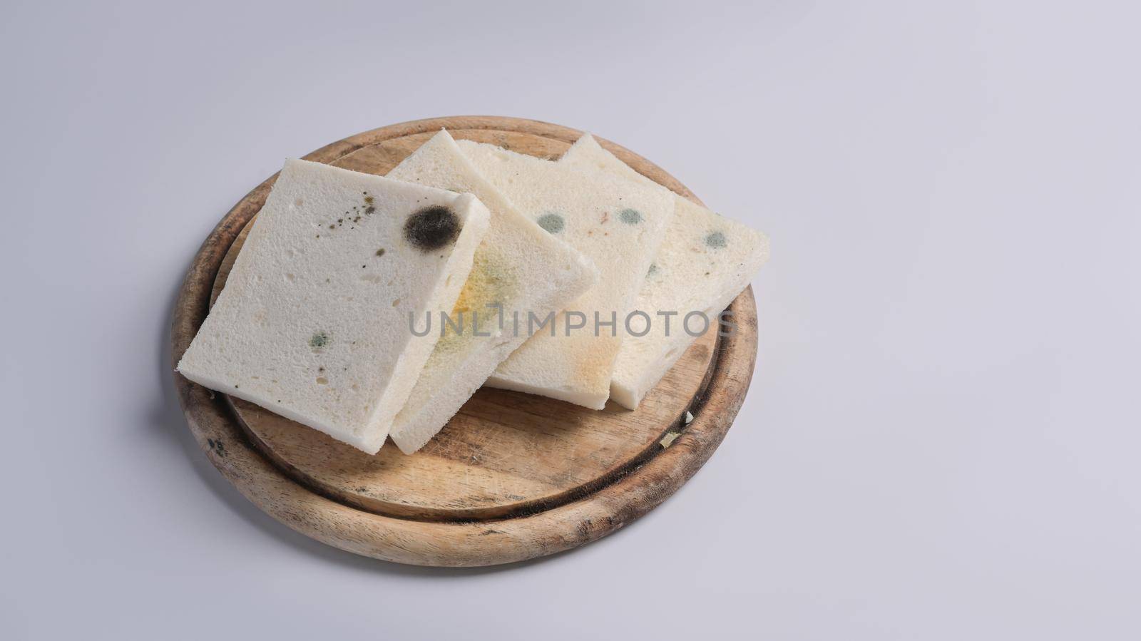 Moldy bread on wooden chopping board with white background.