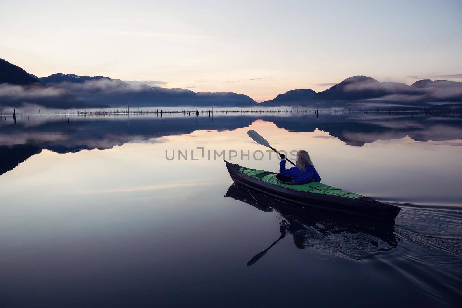 Adventurous Girl kayaking on an infatable kayak in a beautiful lake during a calm and peaceful sunrise. Taken in Stave Lake, East of Vancouver, British Columbia, Canada.