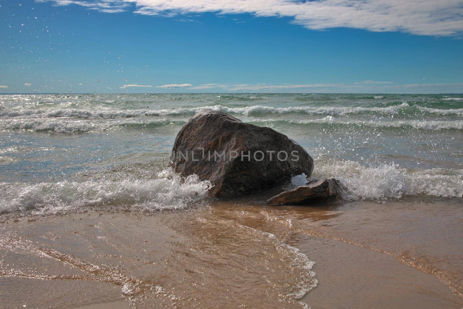 Waves Crash into a Backlit Boulder at a Beautiful Sandy Beach with Blue Skies at Bluewater Beach by markvandam