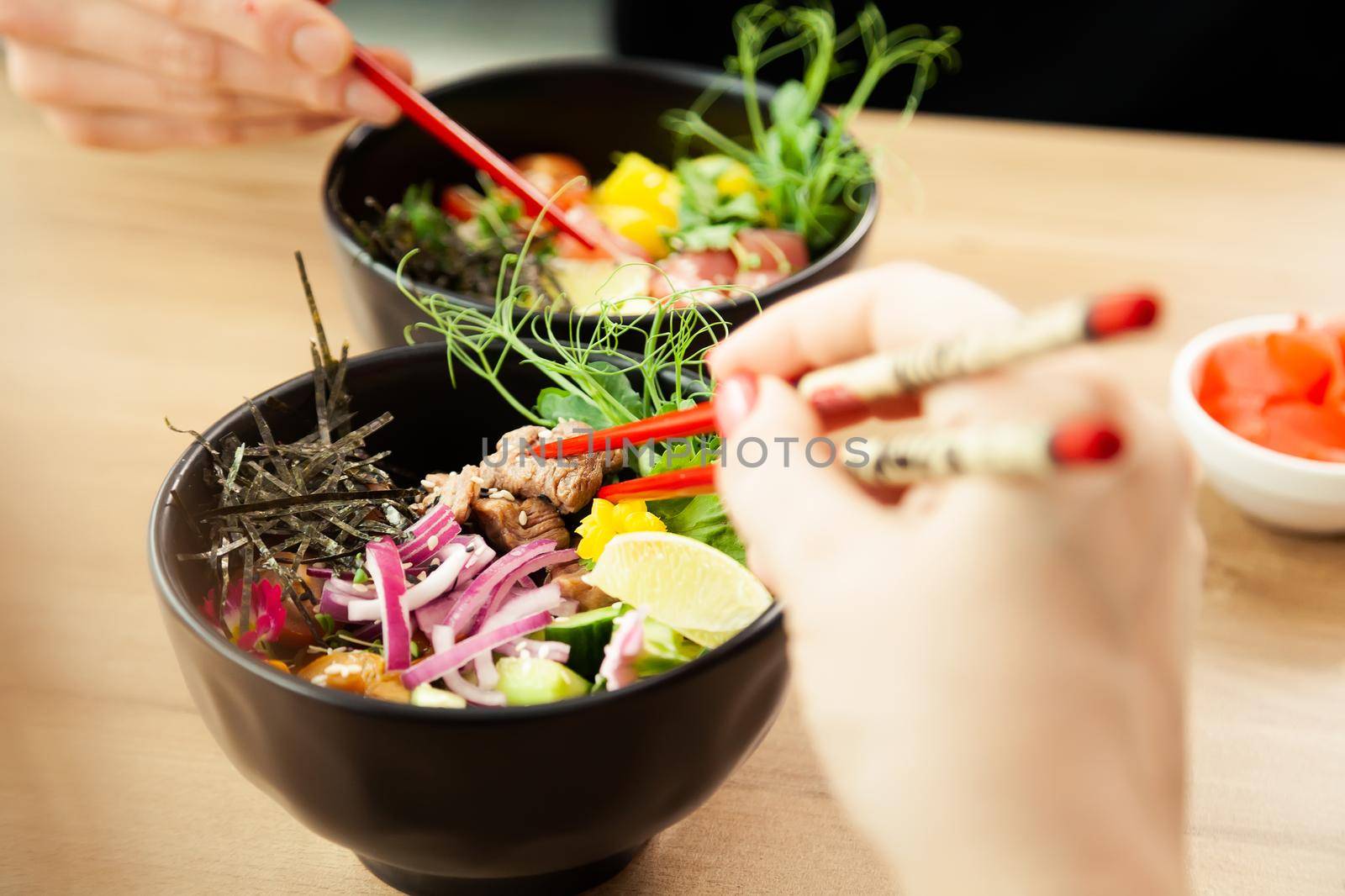 Man and woman eating poke salad with chopsticks. Dab tuna salad in a bowl. People in the restaurant eat salad with chopsticks. Asian seafood salad concept