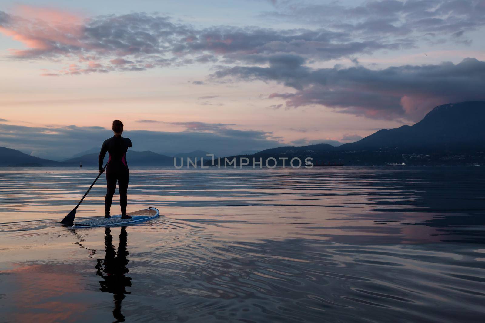 Adventurous girl on a paddle board is paddeling during a bright and vibrant sunset by edb3_16
