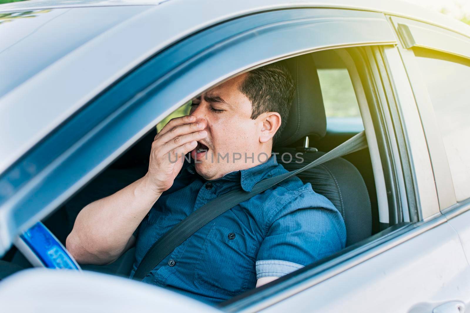 A sleepy driver at the wheel, a tired person while driving, Tired driver yawning, concept of man yawning while driving by isaiphoto