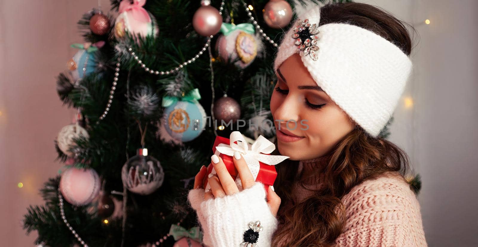 Happy woman holding a gift box on the background of a Christmas tree. Portrait of a happy smiling girl looking at a delivered wrapped box near a decorated fir tree.