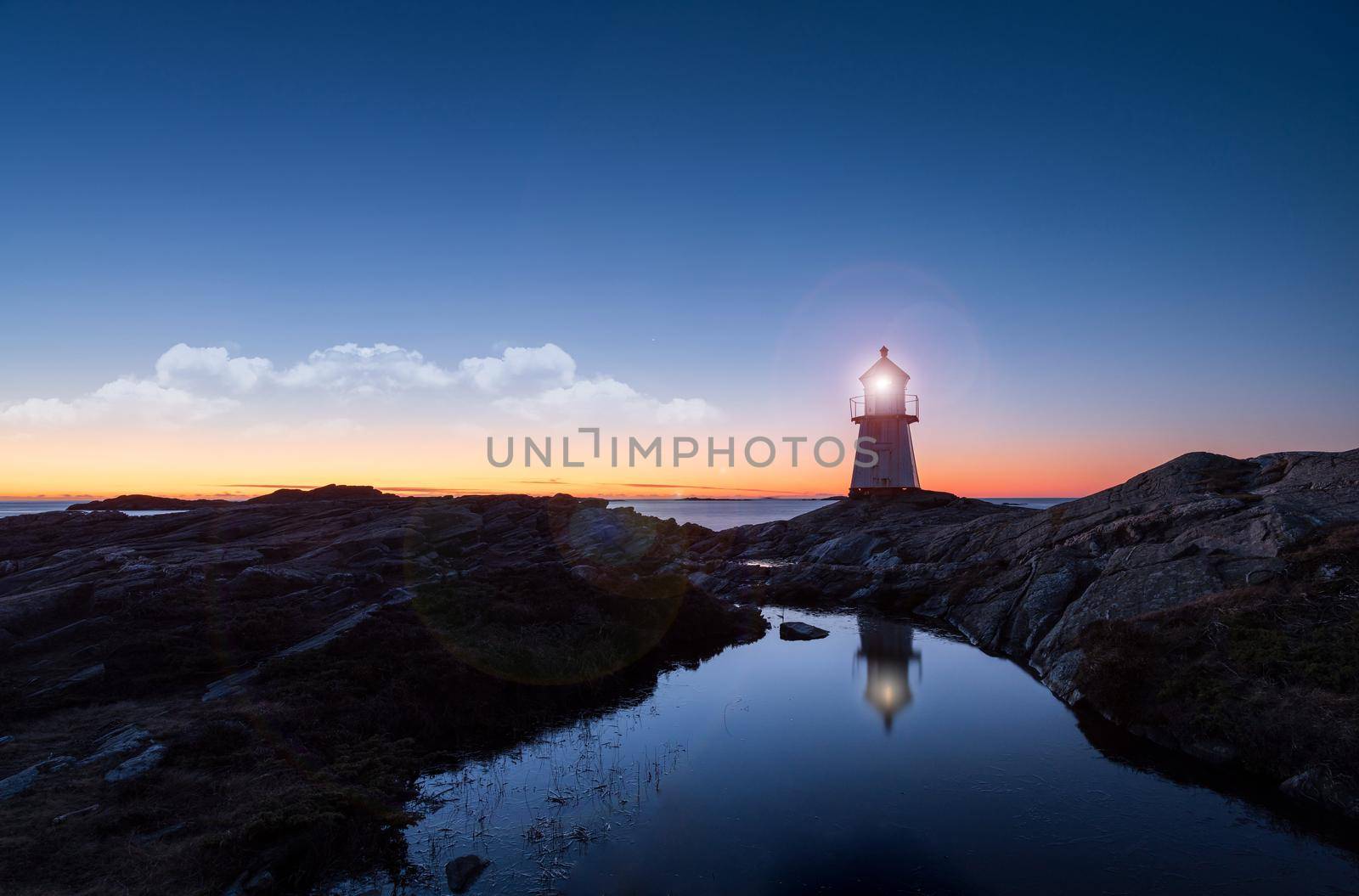 Lighthouse surrounded by rocks at night, lighthouse with lights on at sunset