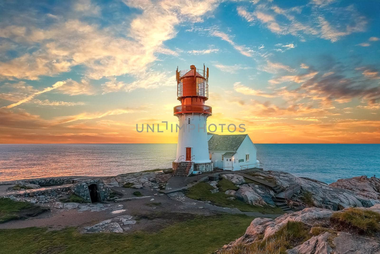 lighthouse surrounded by rocks at sunset, lighthouse surrounded by rocks near the ocean by isaiphoto