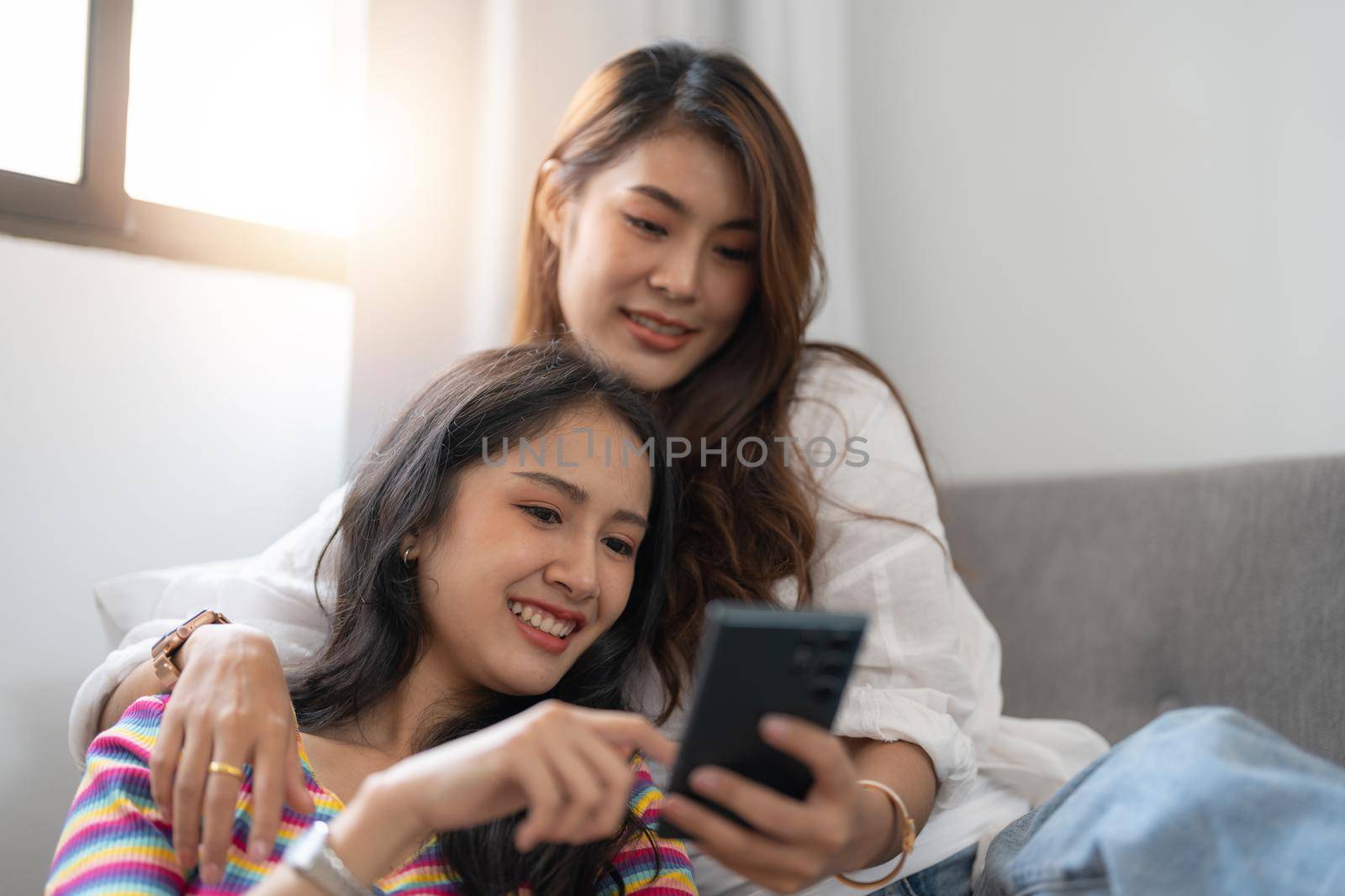 Two happy young asian casual women having fun using smartphone at home. Lesbian millennial couple concept