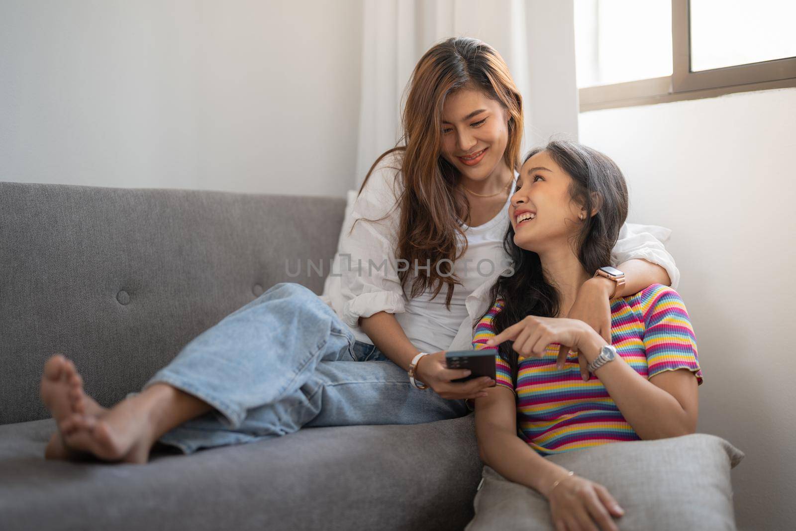 Two happy young asian casual women having fun using smartphone at home. Lesbian millennial couple concept. by nateemee