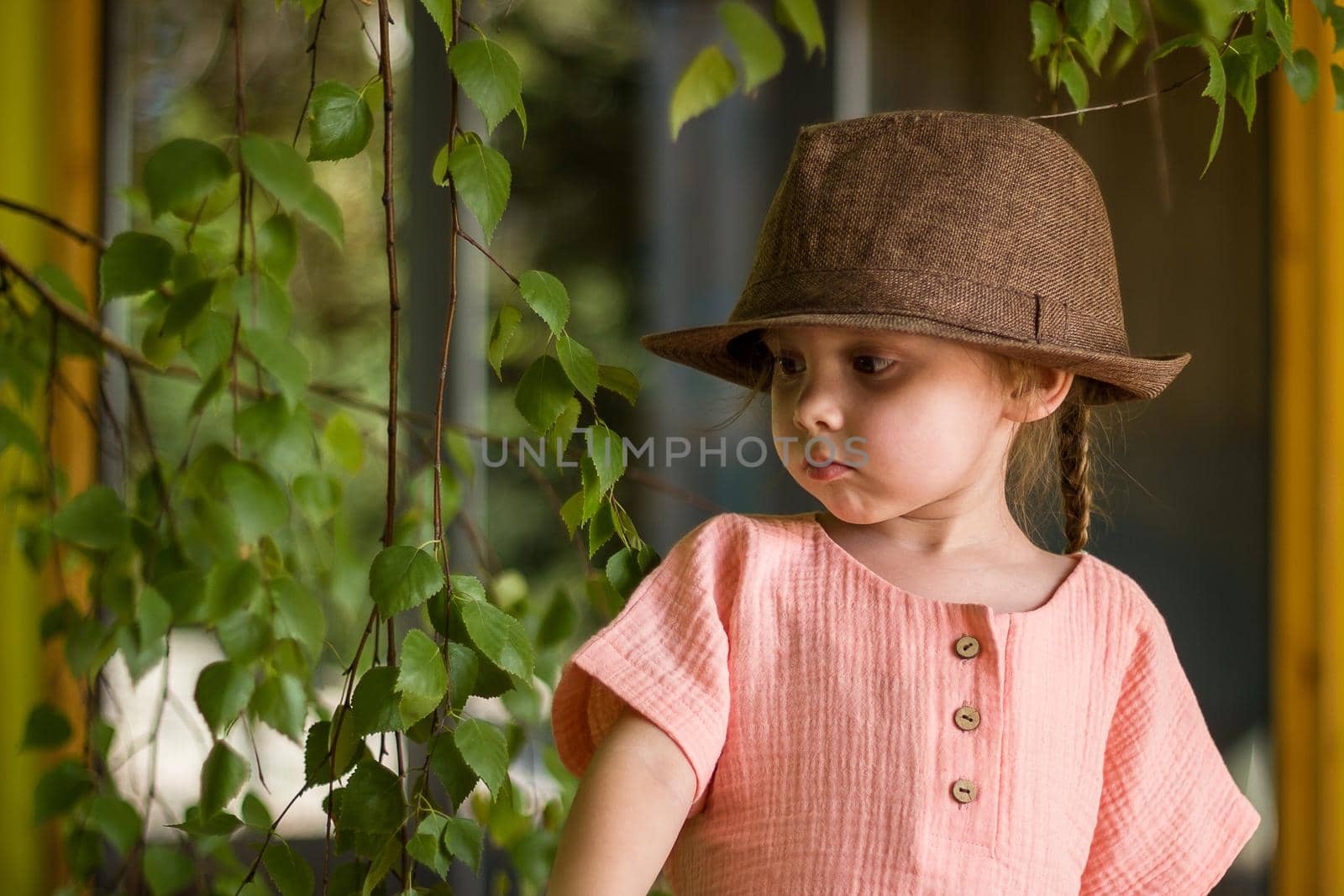 Portrait of happy cute little girl in rural style brown hat and muslin clothes on green background in a summer day.
