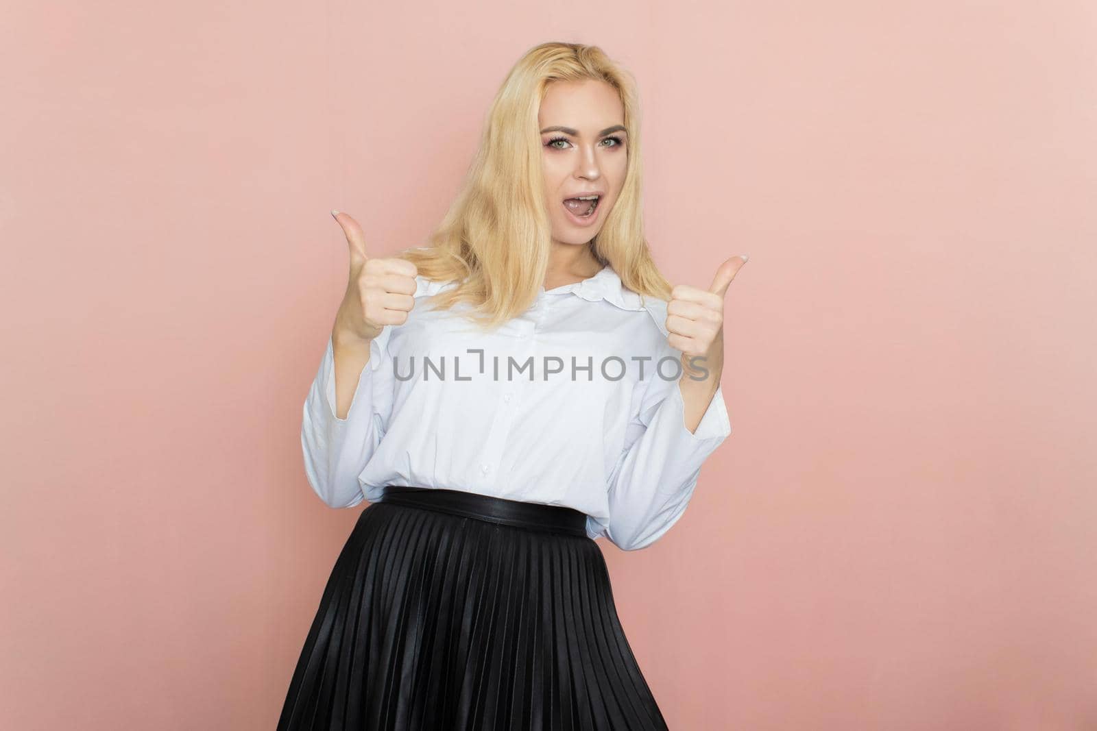 Beauty, fashion portrait. Elegant business style. Portrait of a beautiful blonde woman in white blouse and black skirt posing at studio on a pink background.