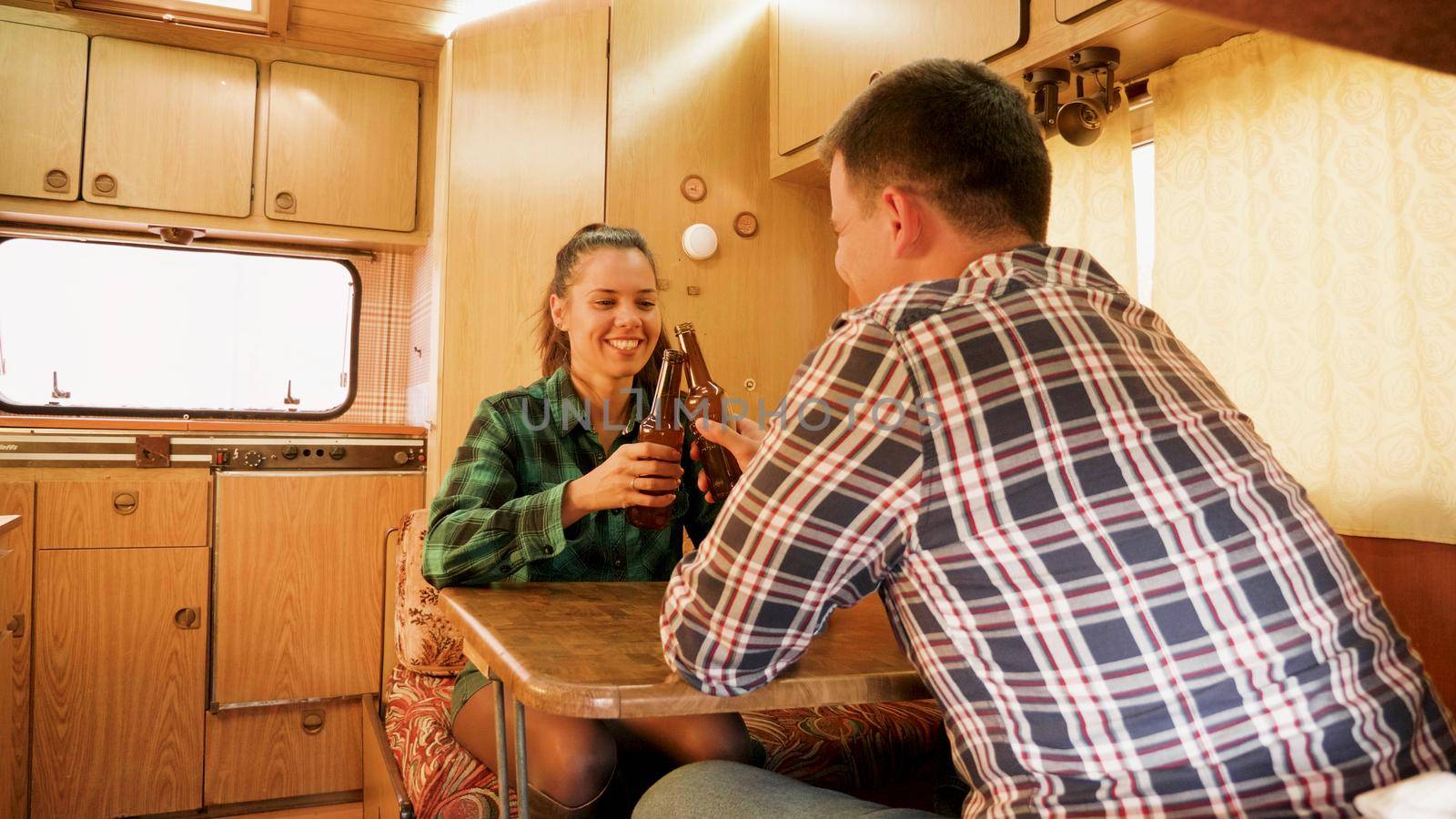 Husbnand making his wife laugh while she's holding a bottle of beer inside of their retro camper van.