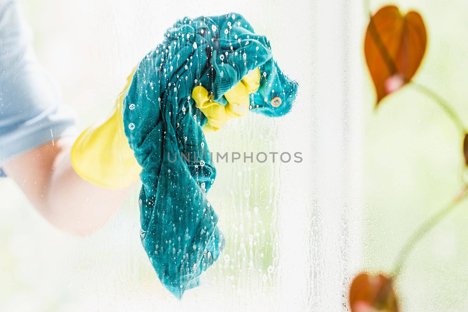 Male hands cleaning house window glass with blue rag. Doing home chores routine