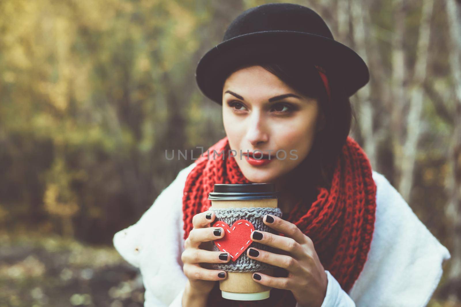 Young woman in a black hat drinks coffee from cozy cup on the nature. Brown toned photo