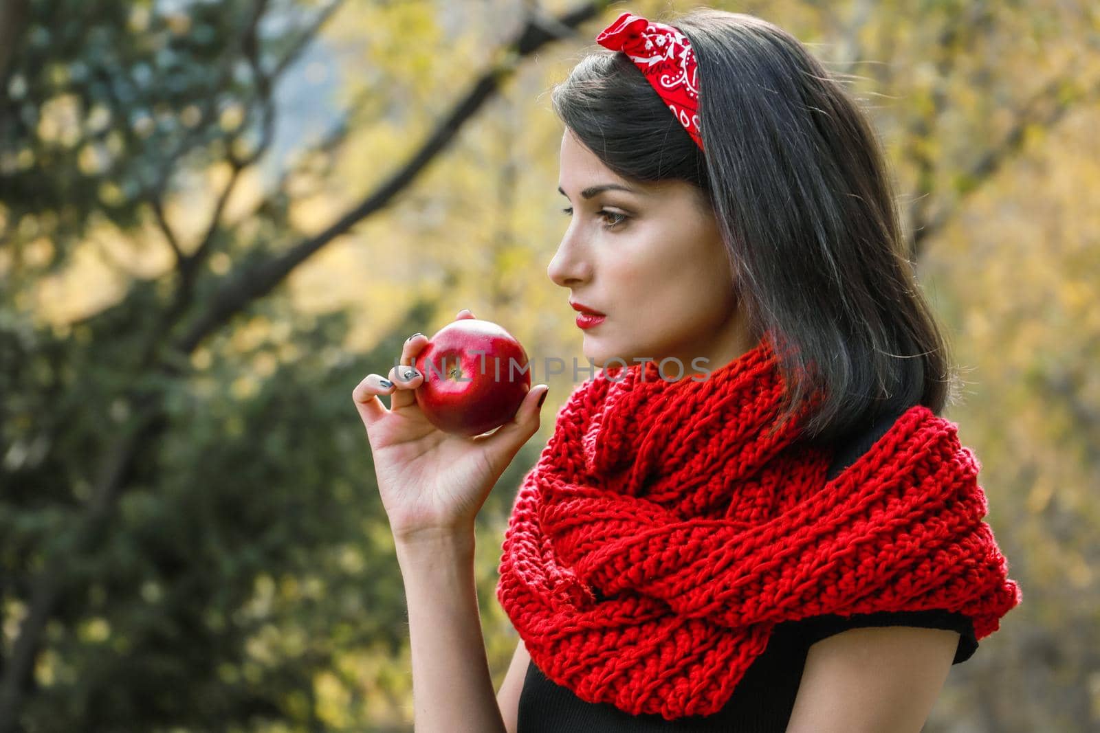 A large ripe apple in a woman hand on a background of a red scarf