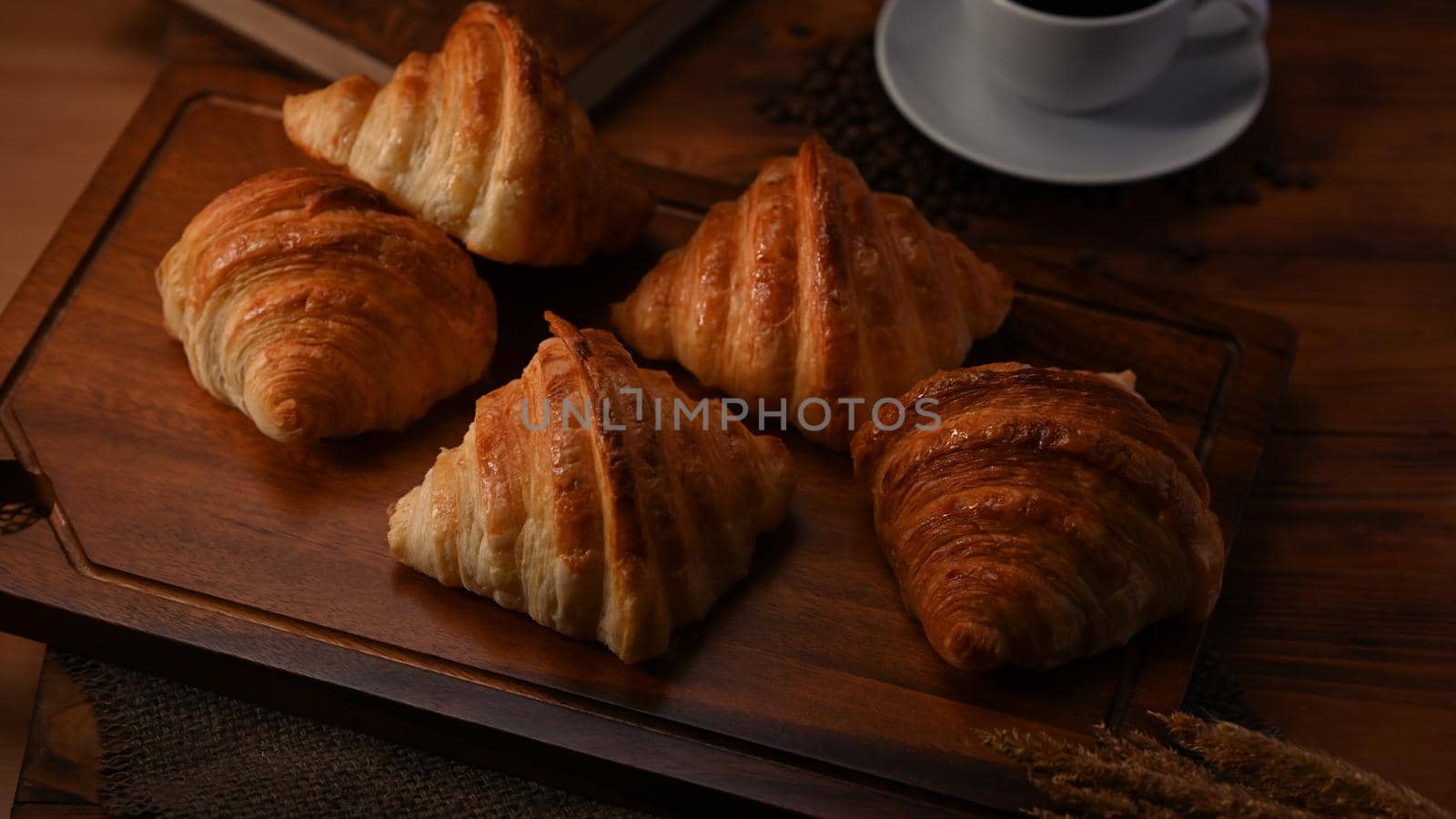 Delicious fresh croissants and coffee cup on wooden board.