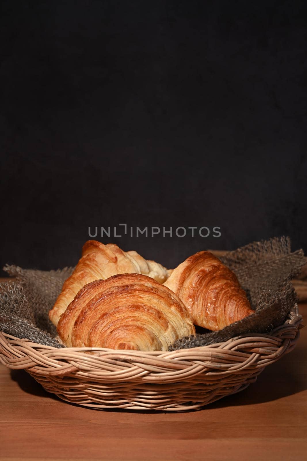 Fresh croissants in a basket on a wooden table for homemade breakfast.