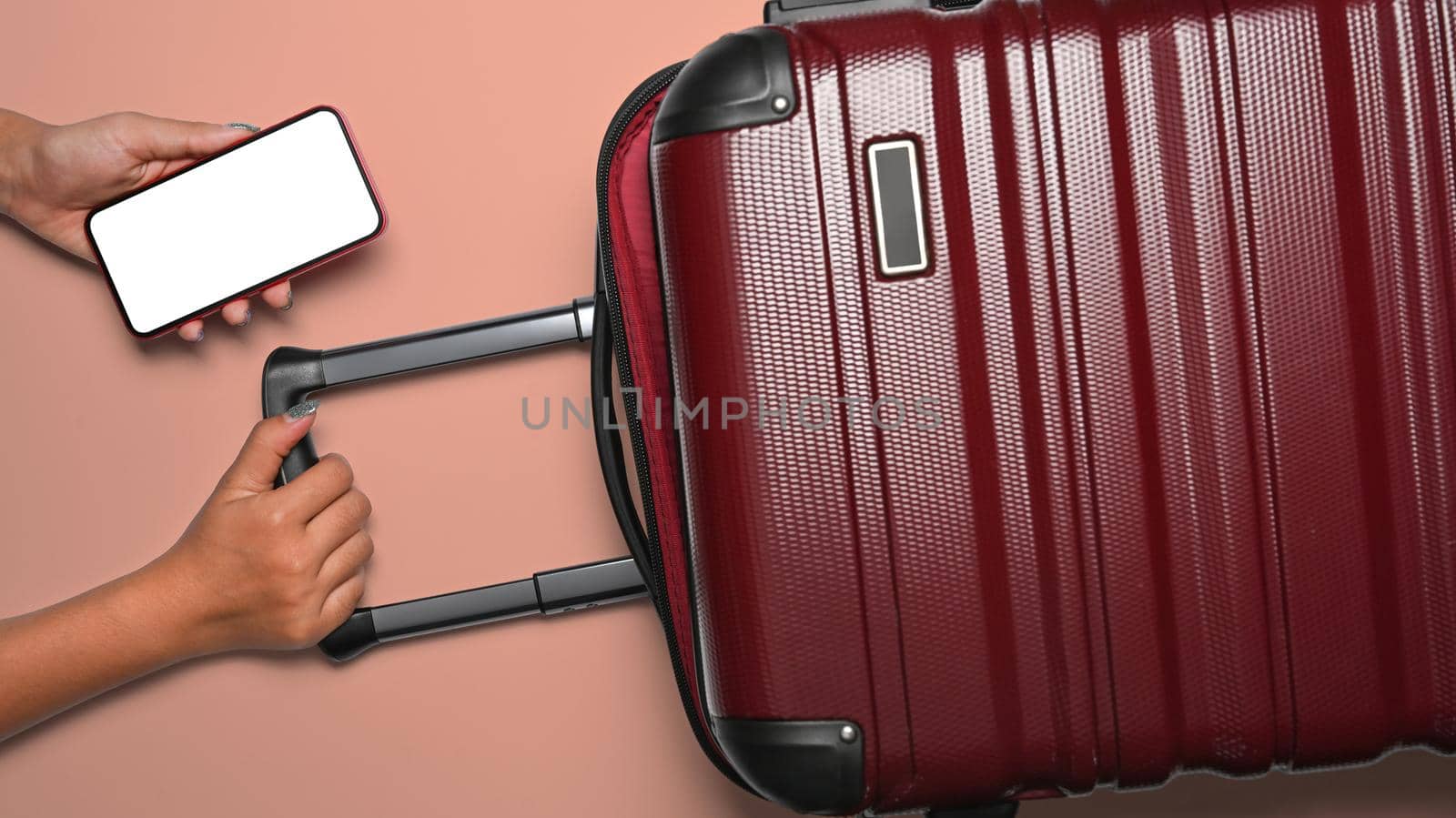 Woman hand holding smart phone and suitcase on pink background. Holidays, travel, tourism, flight luggage concept.