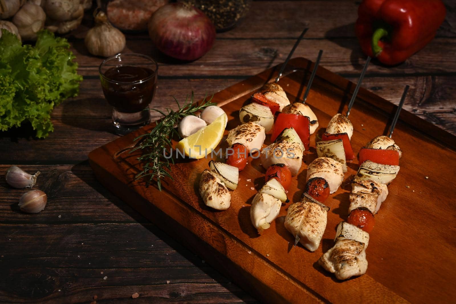 Tasty grilled chicken skewers with spices, herbs and vegetables on cutting board ready to serve.