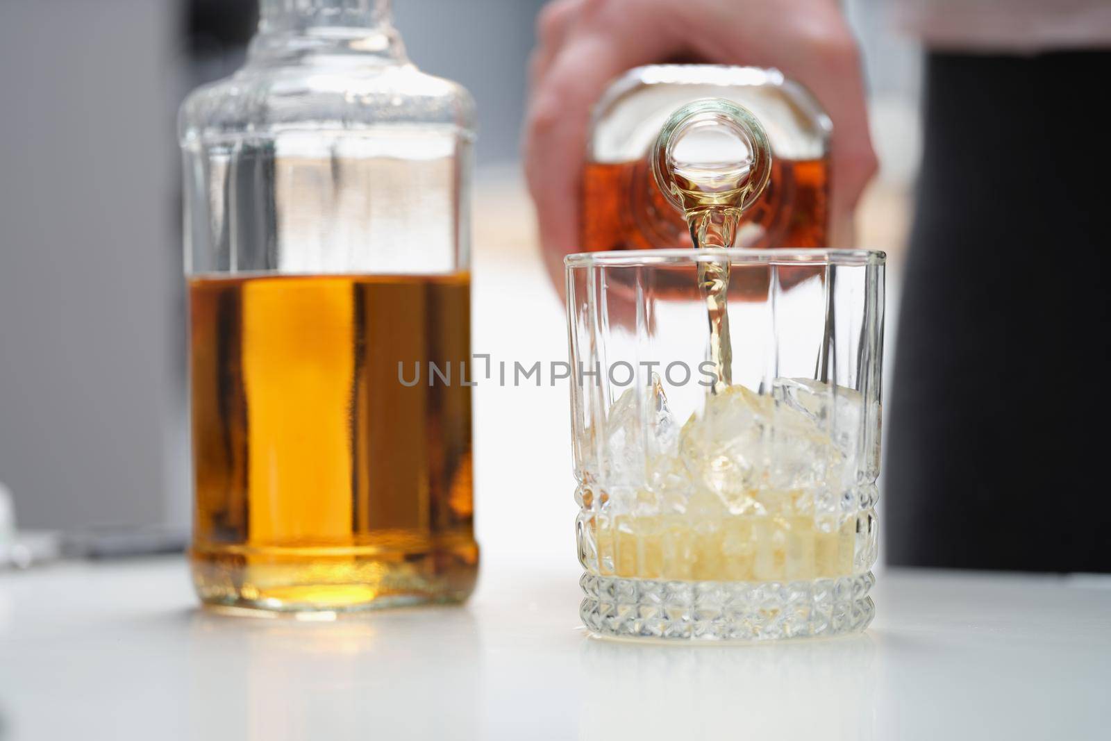 A man pours a strong alcoholic drink into a glass with ice by kuprevich