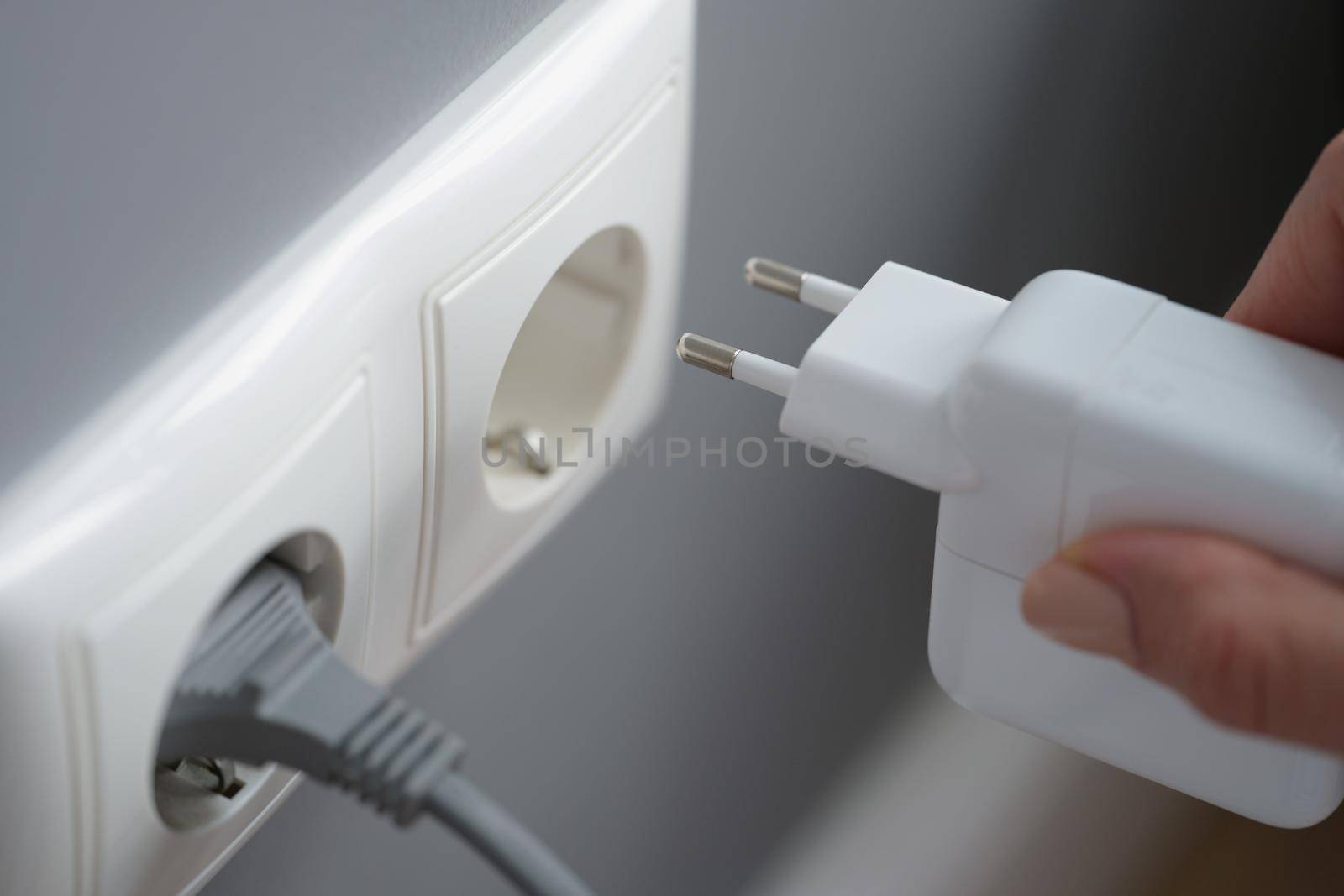 A female hand plugs the power supply unit for a laptop into an outlet, close-up. Uninterruptible power supply, phone charger