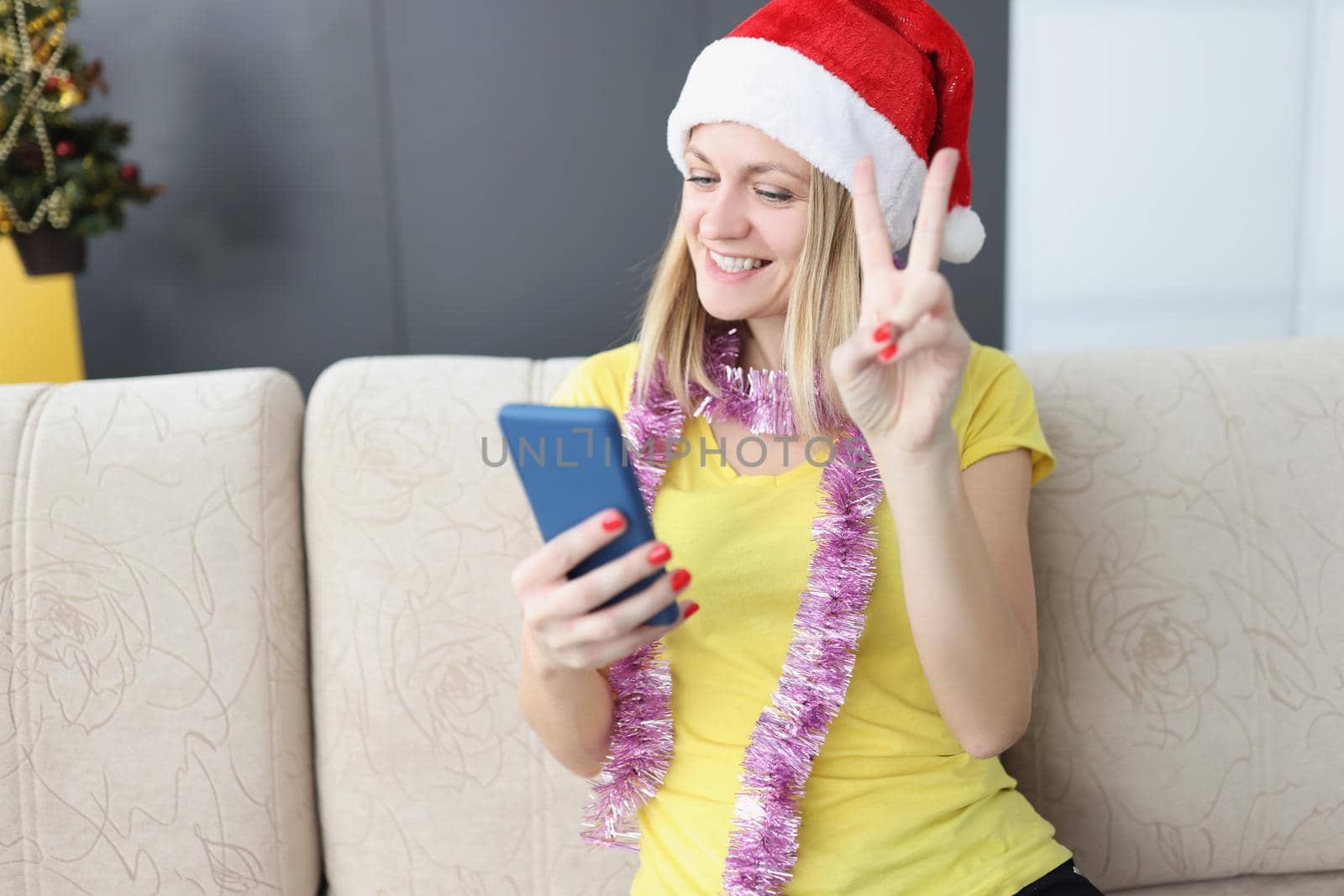 Portrait of smiling blonde woman show peace sign on smartphone, talk to friend or family on video call, congratulate with new year holiday. Christmas, technology, connection concept