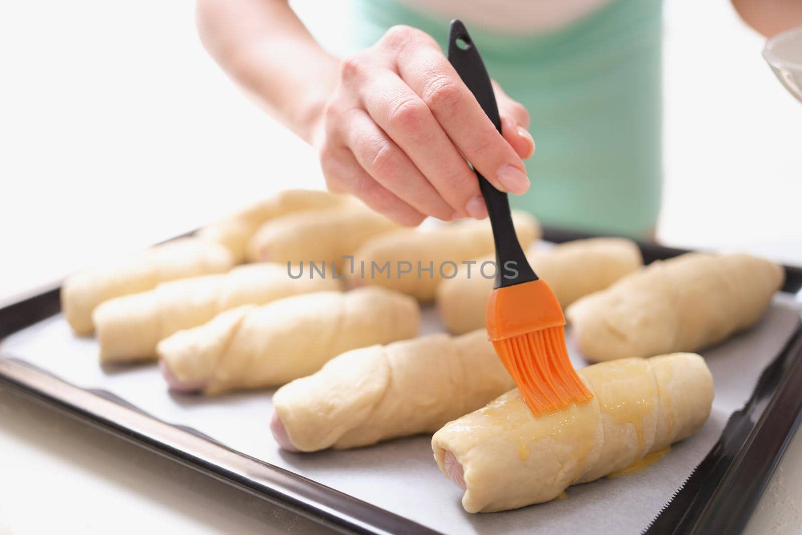 A woman before baking with a brush lubricates dough products, close-up. Delicious homemade cakes, family meal preparation
