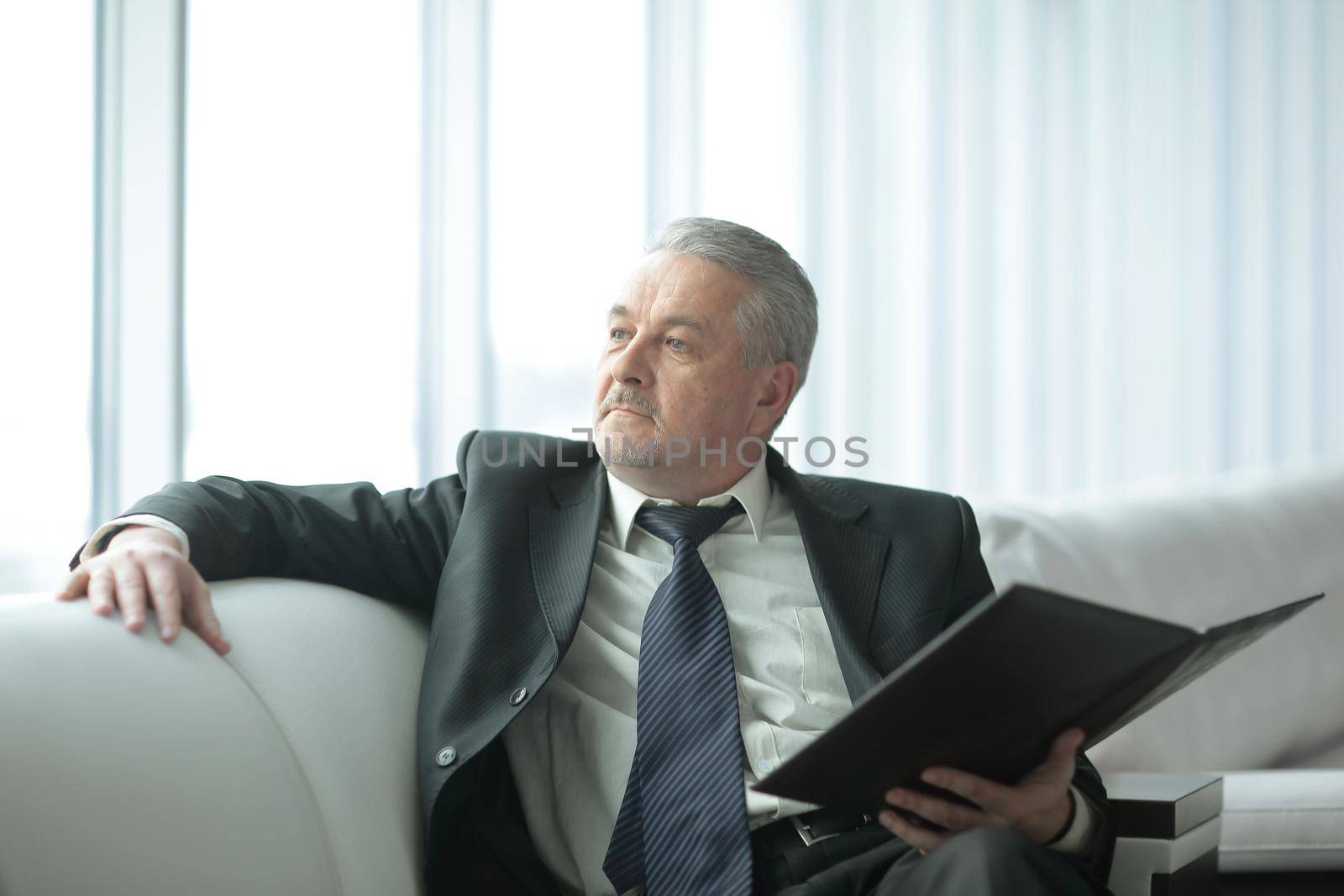 pensive businessman with clipboard sitting on the office couch.