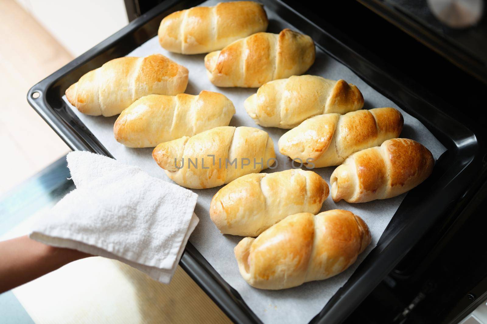 A woman takes buns out of the oven on a baking sheet, close-up. Homemade bread, baking at home, organic food