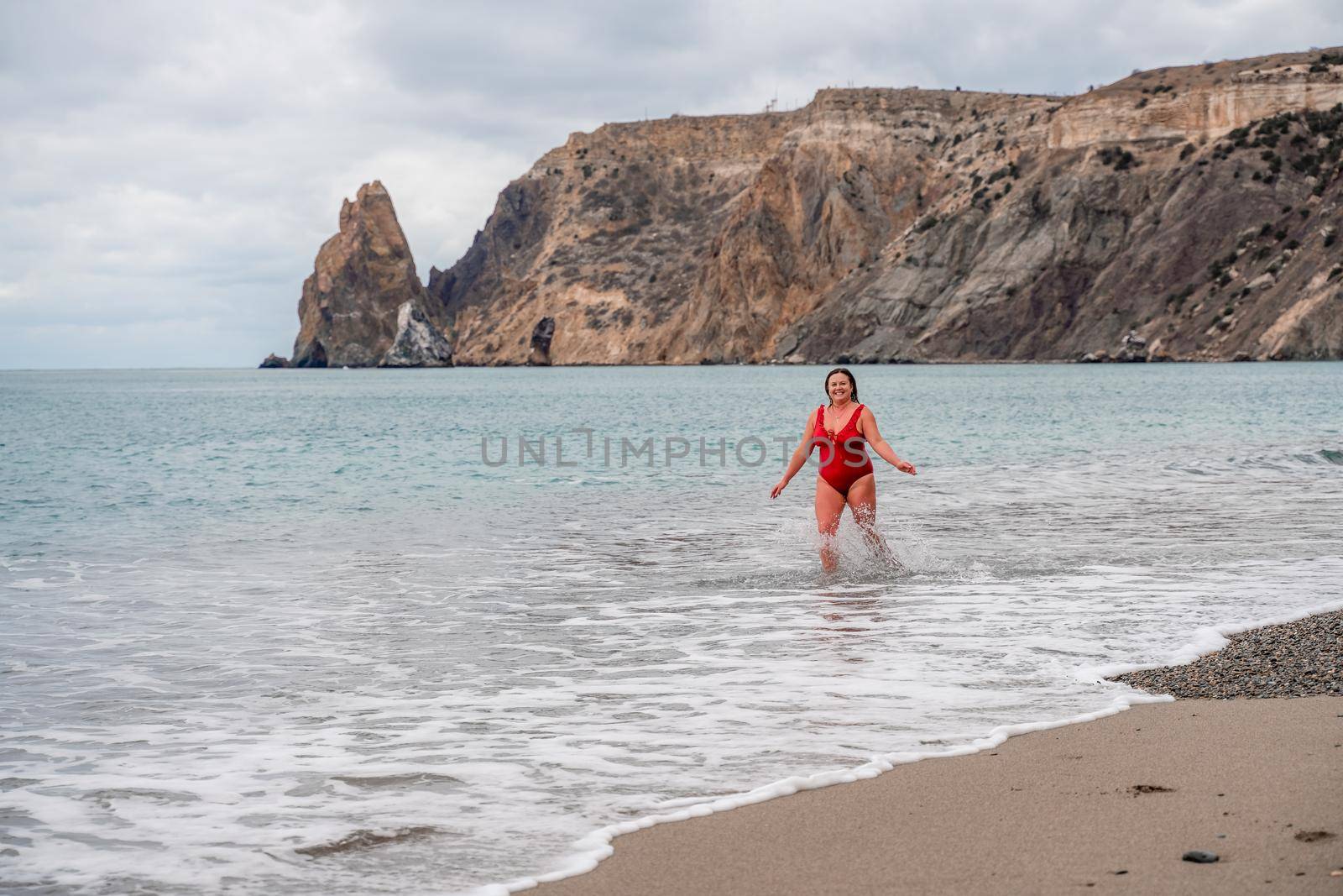 Woman in a bathing suit at the sea. A fat young woman in a red swimsuit enters the water during the surf by Matiunina