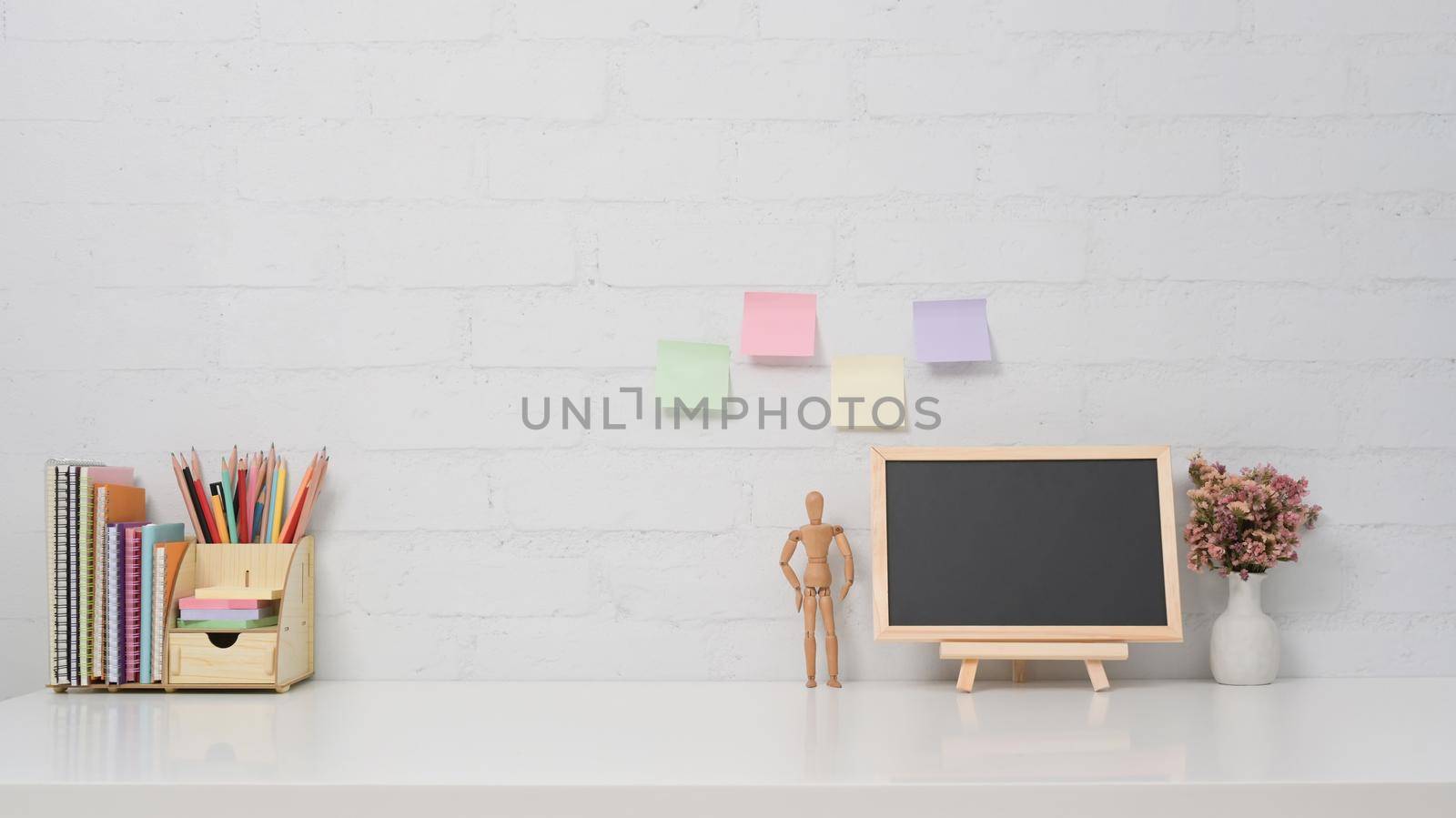 Chalkboard, potted plant and stationery on white table against brick wall. Copy space for your information content.