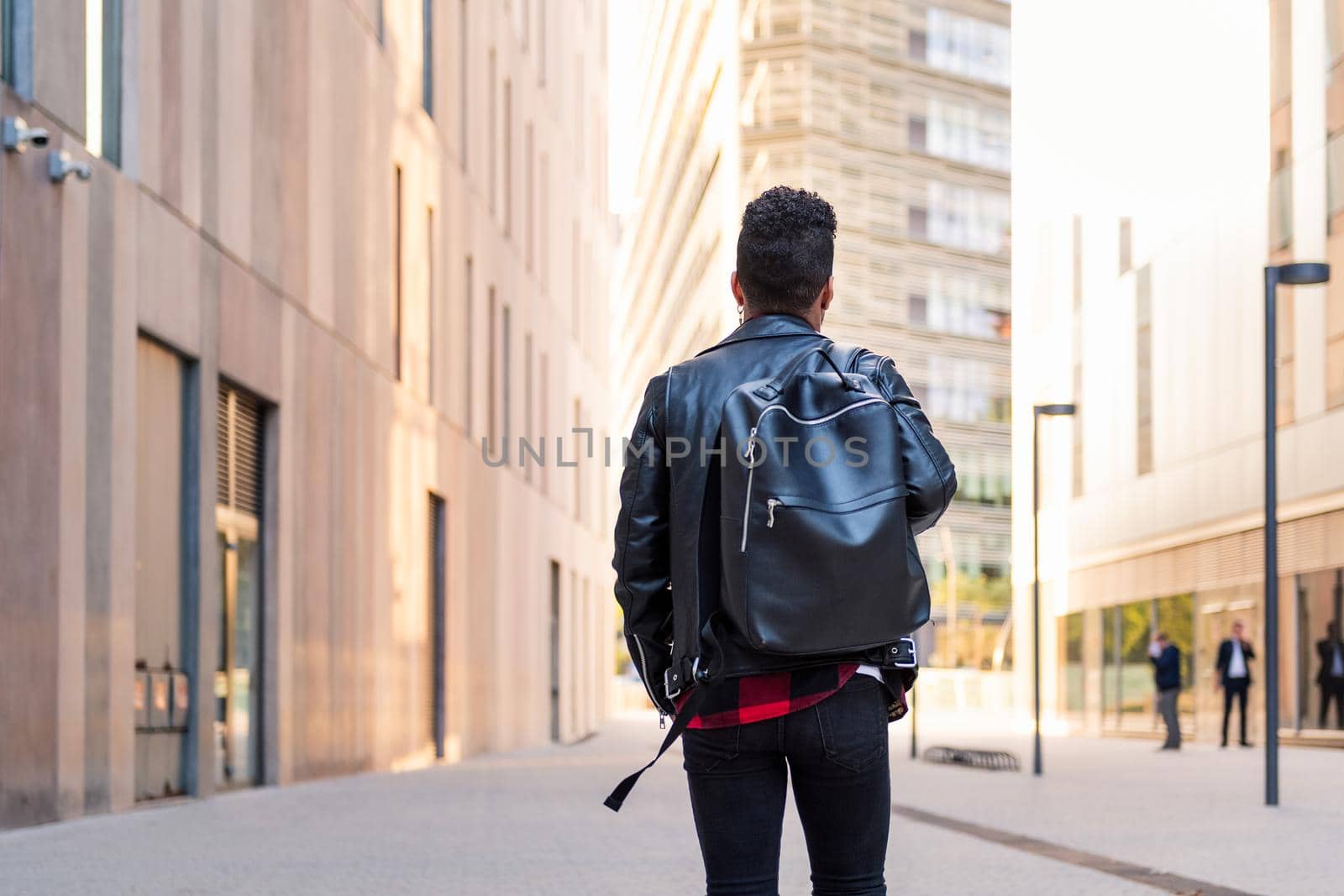 rear view of a stylish young student with backpack walking in the city, concept of urban lifestyle