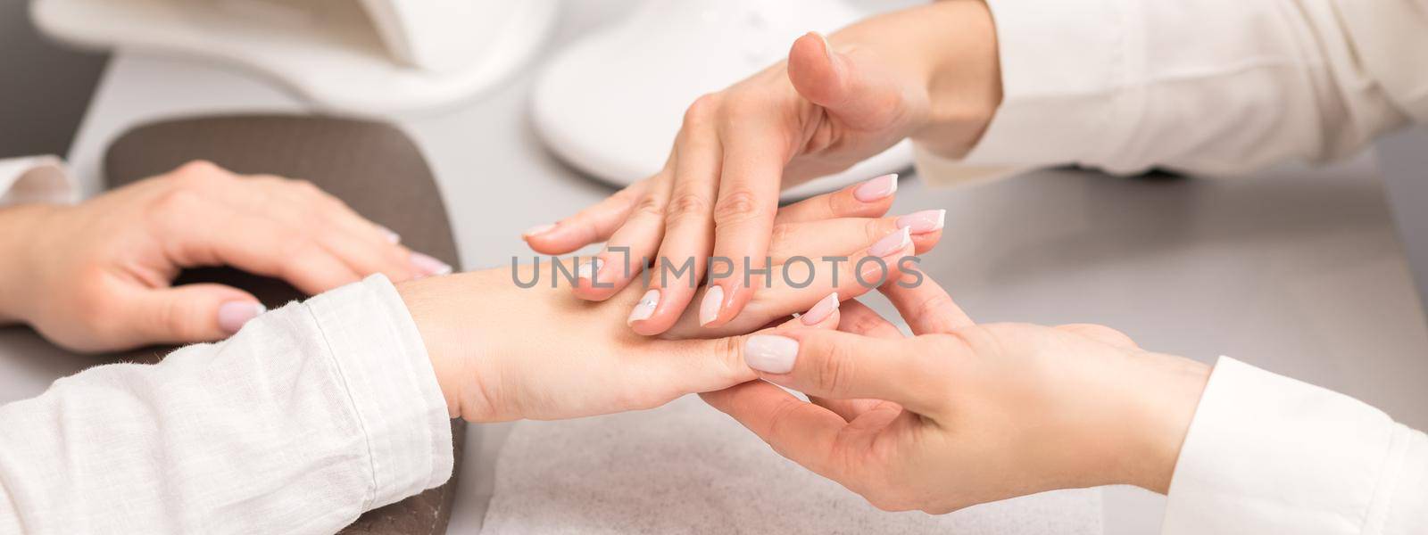 Hands and nails of young woman receiving oil massage by beautician at beauty salon.