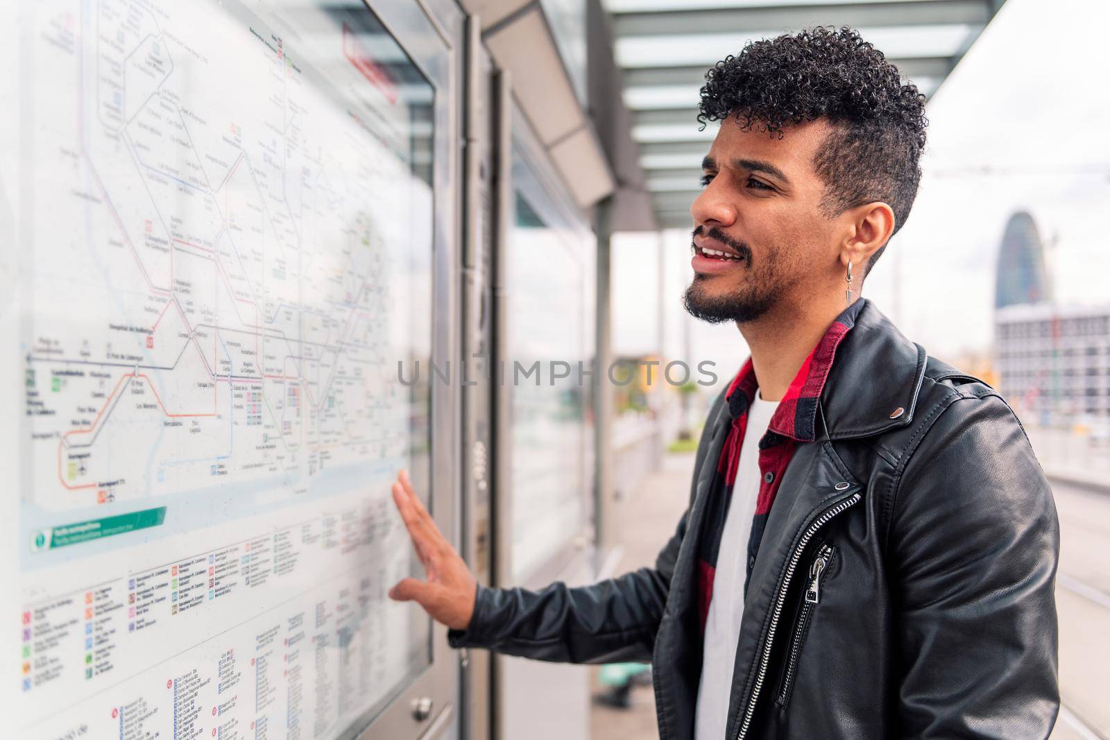 stylish young latin man consulting the public transportation map at the bus stop, concept of sustainable transportation and urban lifestyle